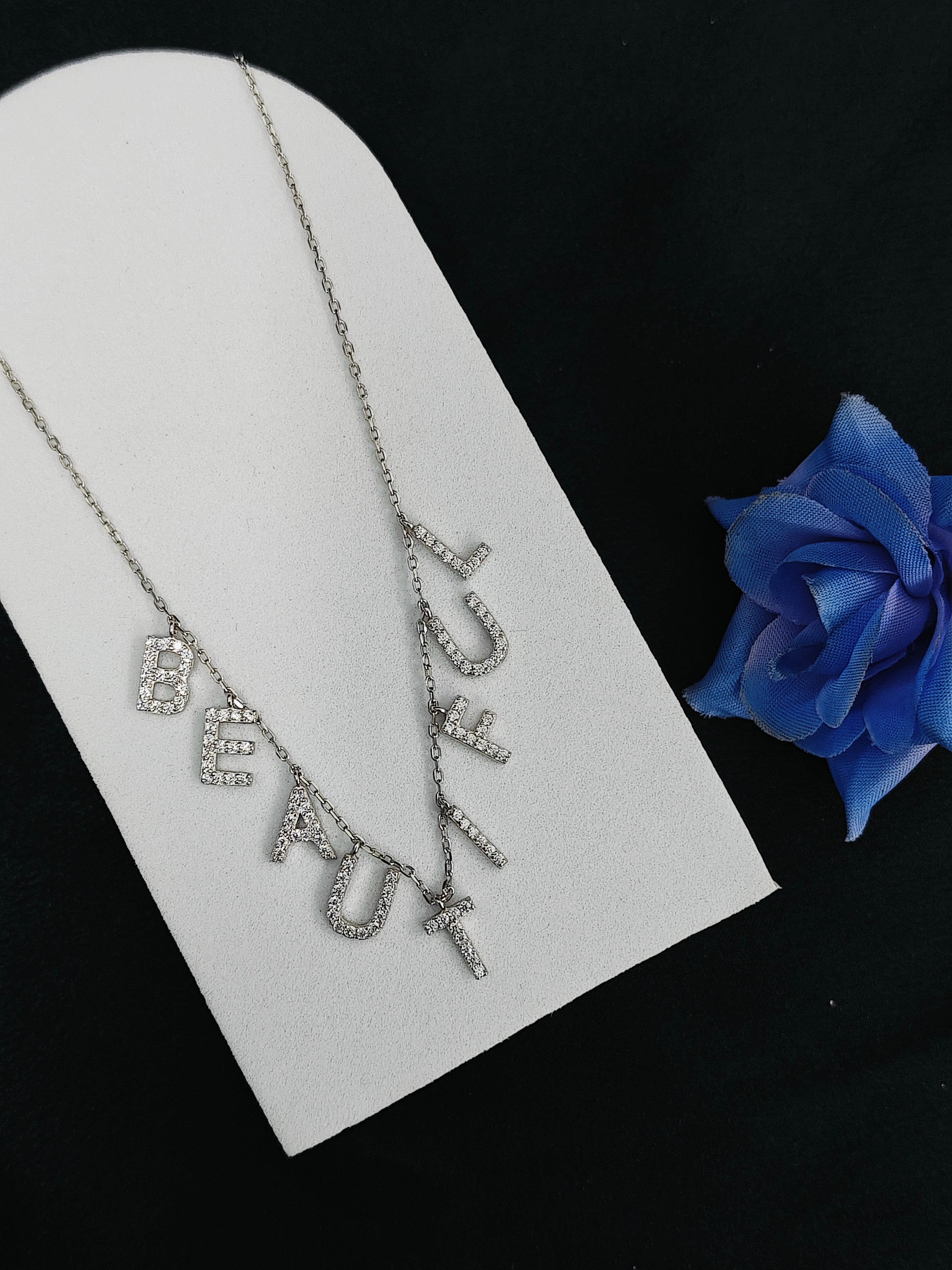 Silver necklace with 'BEFAUX' pendant on a white card with a blue rose.